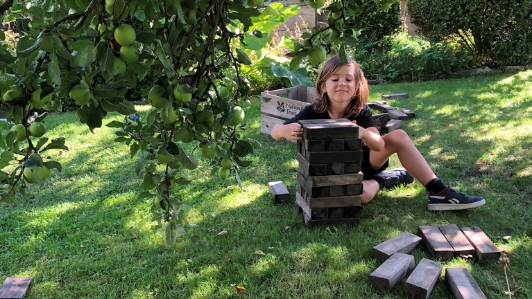 A young boy playing lawn jenga under an apple tree in the garden